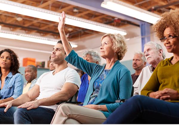 Photo of an audience, one person has their hand raised